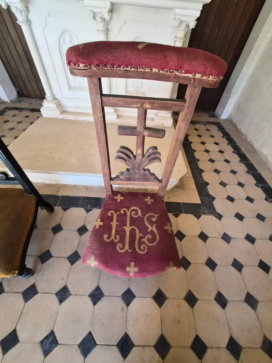 À l'intérieur de la chapelle : le sol de carreaux, le coussin brodé du monogramme IHS et la croix de procession.
