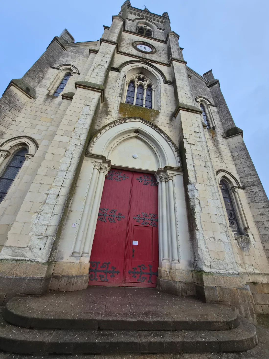 La façade néo-gothique de l'église Saint-Pierre-et-Saint-Paul de Freigné et sa grande porte rouge, sous le clocher de 51 mètres.