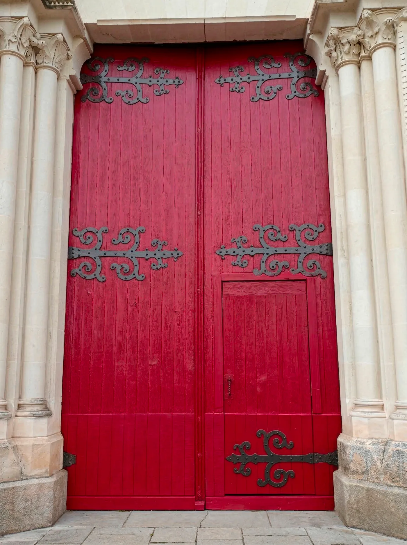 La grande porte de l'église, restaurée : ses ferrures ouvragées et son rouge profond retrouvés, encadrées par les colonnettes néo-gothiques en tuffeau.