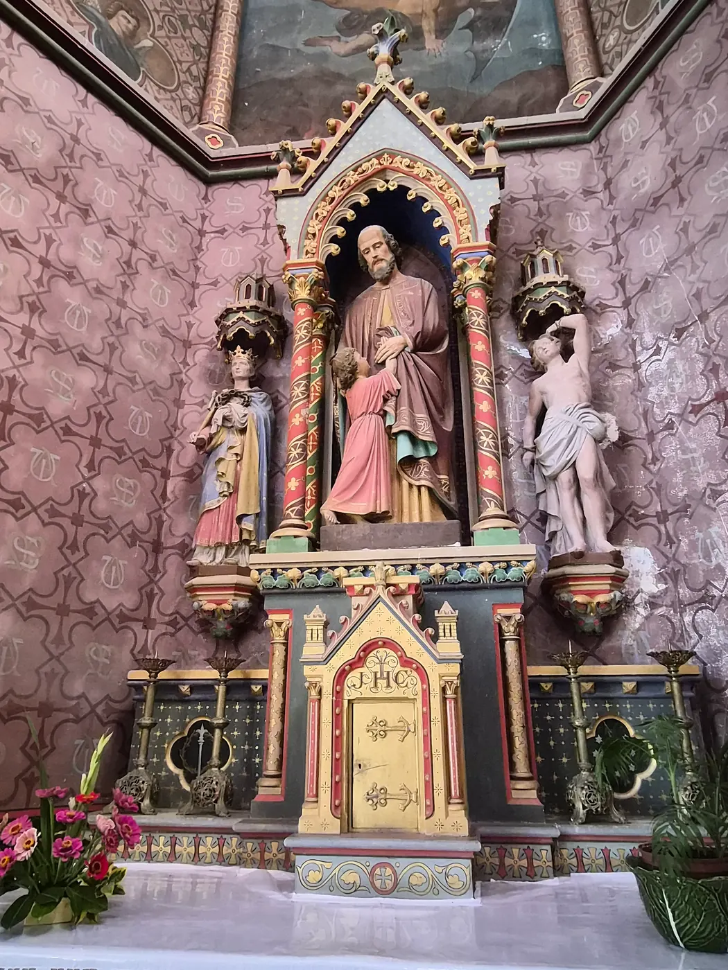 Le retable polychrome d'une chapelle latérale et ses statues, sur fond de murs peints.