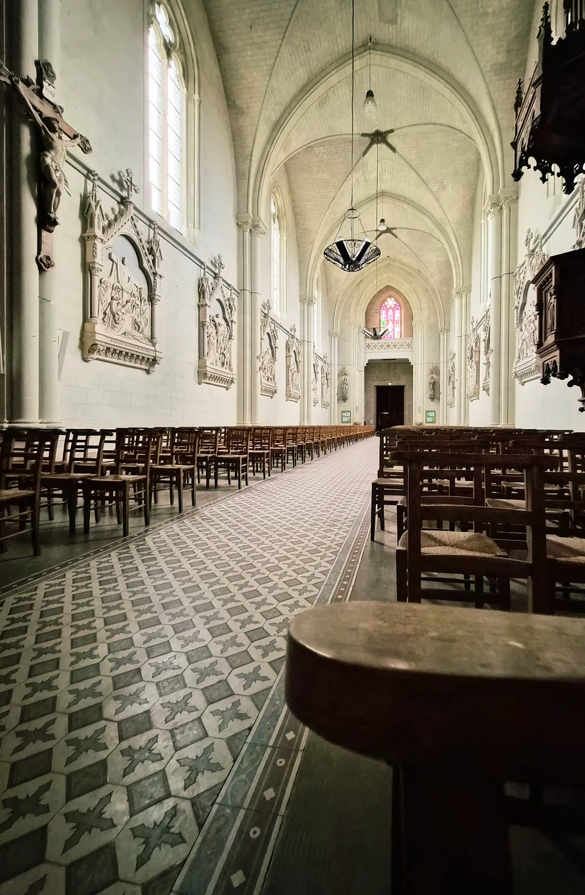 L'intérieur de l'église de Freigné : la nef néo-gothique, ses voûtes, le chemin de croix en bas-relief et le sol en carreaux de grès émaillé.