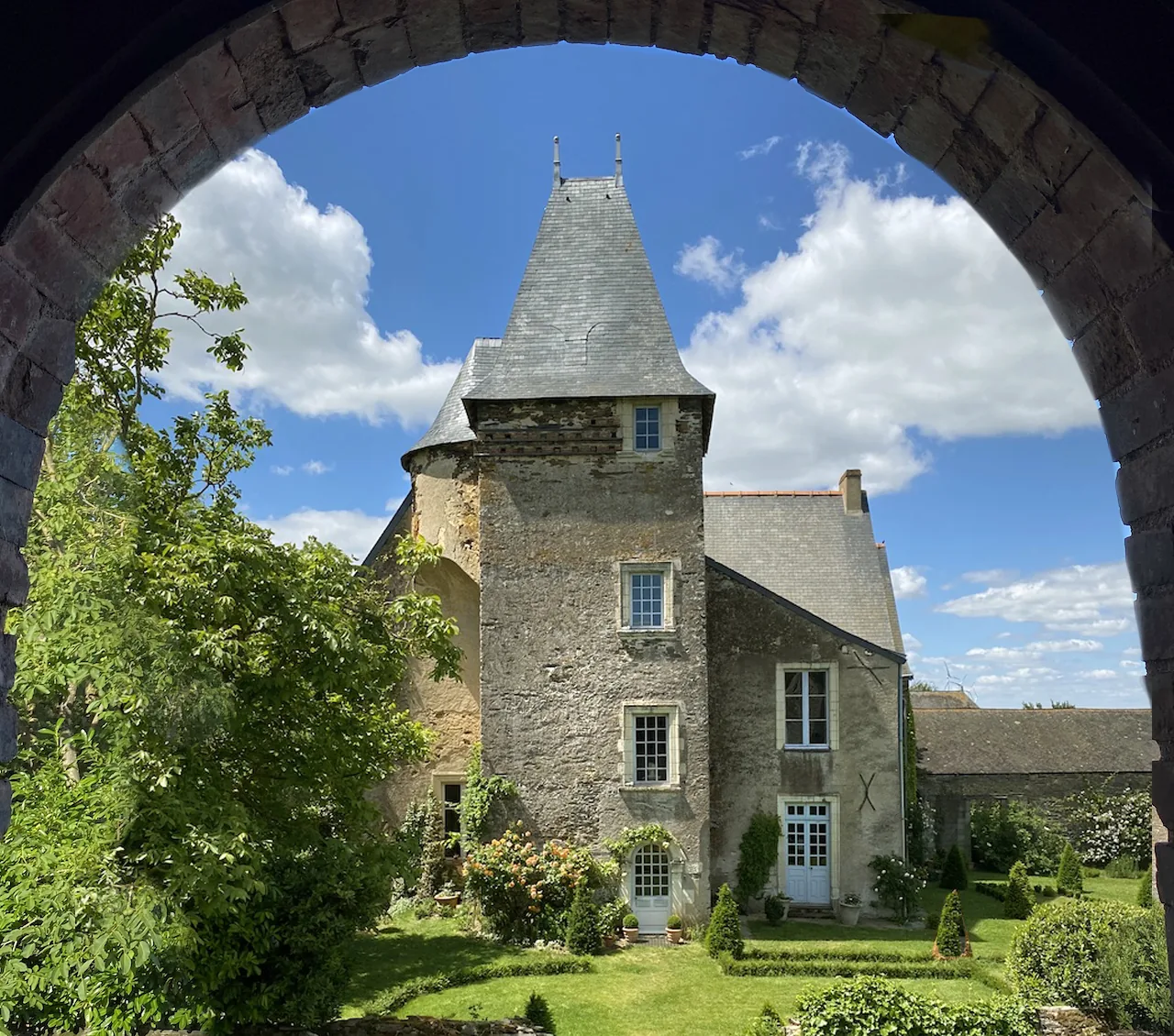 Le manoir de Ghaisne encadré par une arche de pierre du jardin. La tour d'escalier occupe le centre du logis ; la petite ouverture ménagée sous le toit en pavillon éclaire l'ancienne chambre du guetteur.