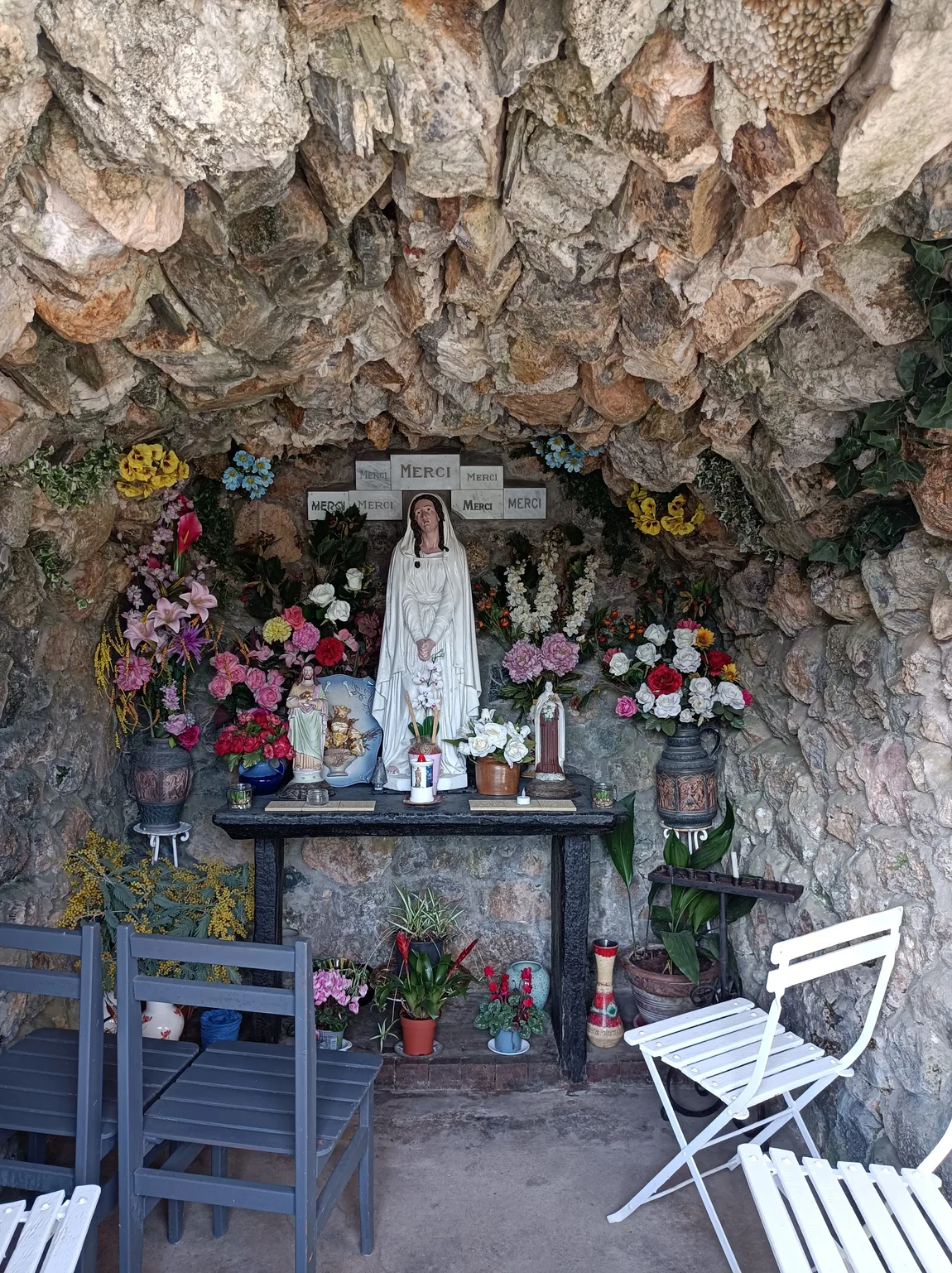 L'intérieur de la grotte : Notre-Dame de Pitié entourée de fleurs et d'ex-voto « MERCI », témoins d'une dévotion toujours vivante.