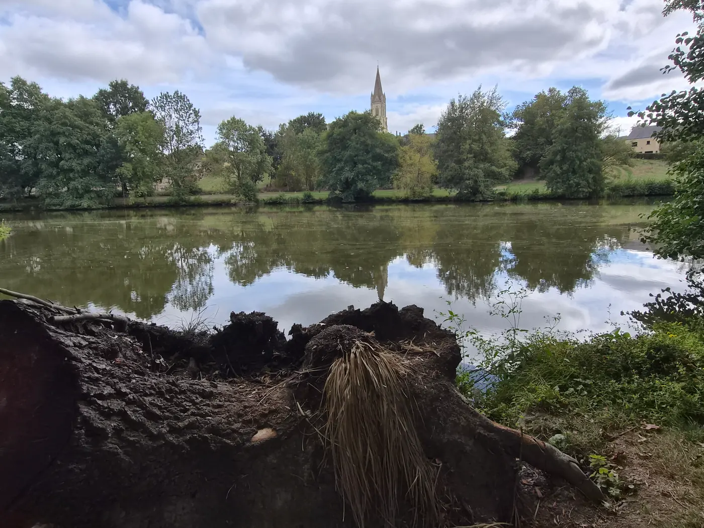 Depuis la rive, le clocher de l'église Saint-Pierre-et-Saint-Paul se reflète dans le plan d'eau (septembre 2026).