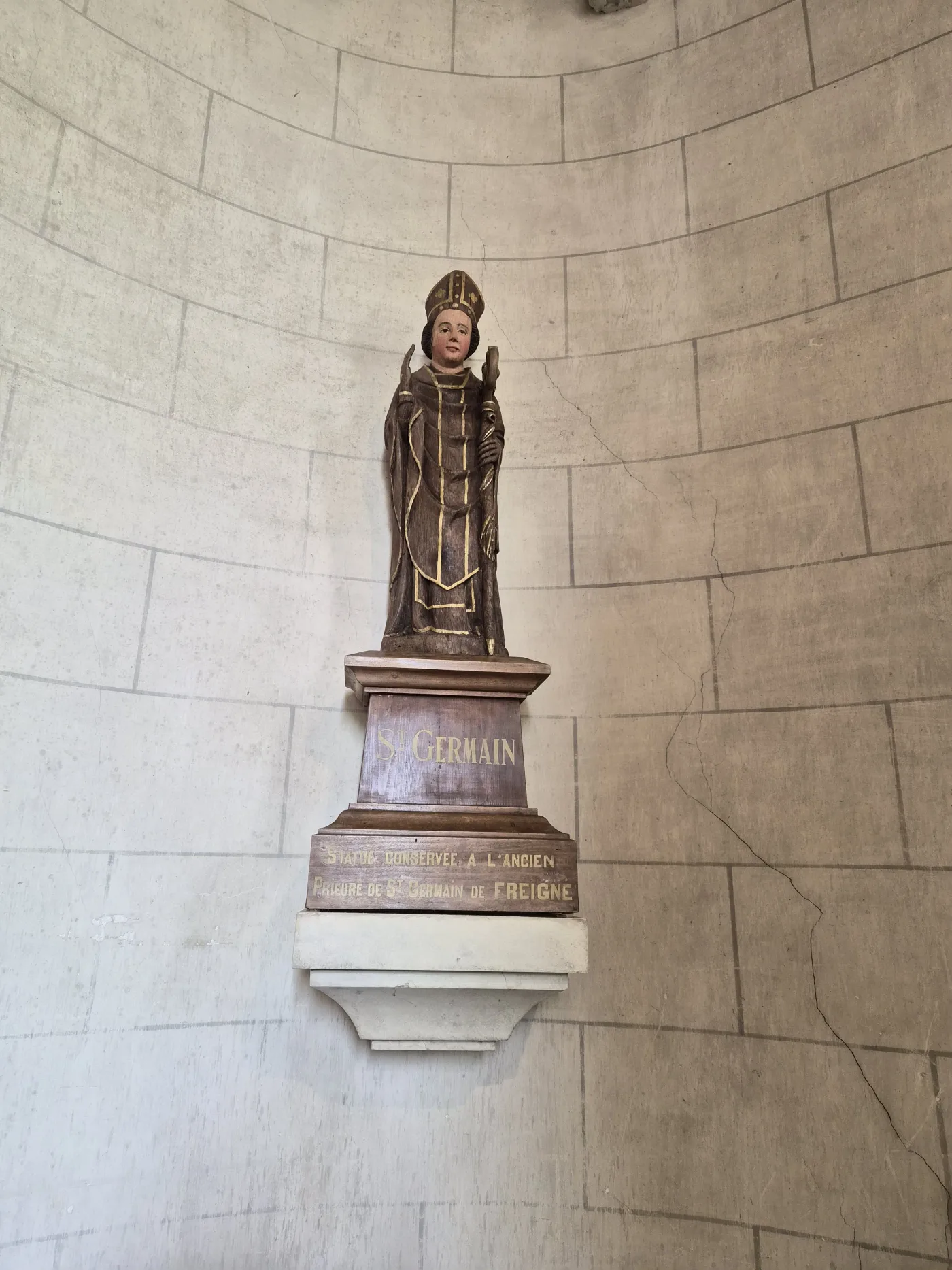 Saint-Germain, crosse d'évêque en main, sur son socle : « Statue conservée à l'ancien prieuré de Saint-Germain de Freigné ».